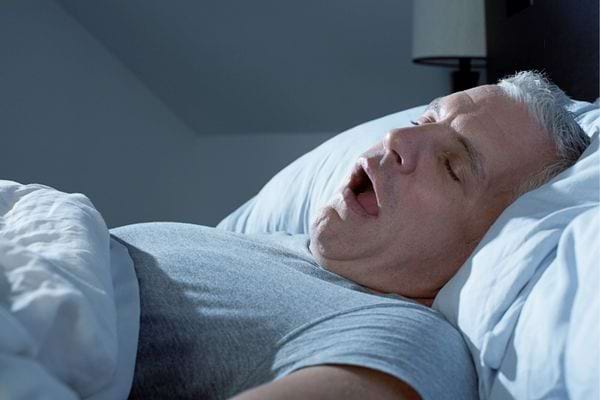 Homme &acirc;g&eacute; dormant sur le dos la bouche ouverte dans un lit.