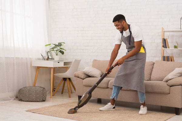 Un homme souriant passe l aspirateur sur un grand tapis beige dans le salon.