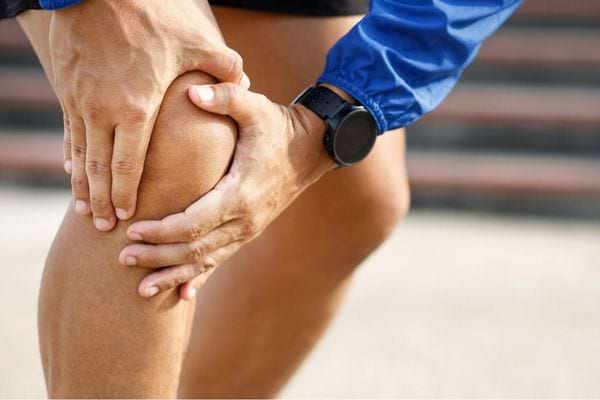 Homme tenant son genou douloureux en position de coureur.