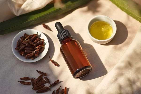 Flacon ambré d’huile naturelle entouré de clous de girofle séchés et d’un petit bol d’huile dorée.