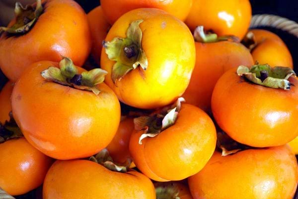 Tas de kakis mûrs à la peau orange brillante.