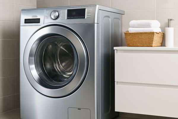 Une machine à laver argentée est installée dans une salle de bain propre.