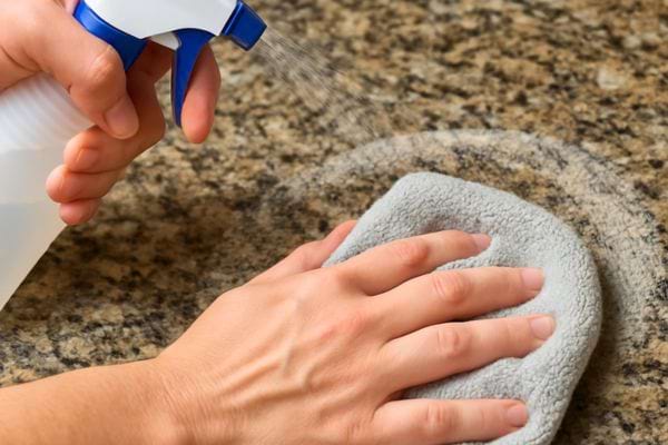 Main vaporisant un produit sur un comptoir en granit tandis qu'un chiffon essuie la surface.