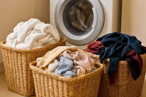 Trois paniers remplis de v&ecirc;tements tri&eacute;s devant une machine &agrave; laver.