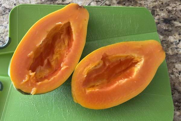 Papaye ouverte en deux sans graines sur une planche verte.