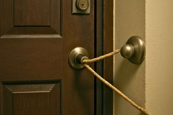 Une porte est solidement bloquee avec une corde attachee entre deux poignées.