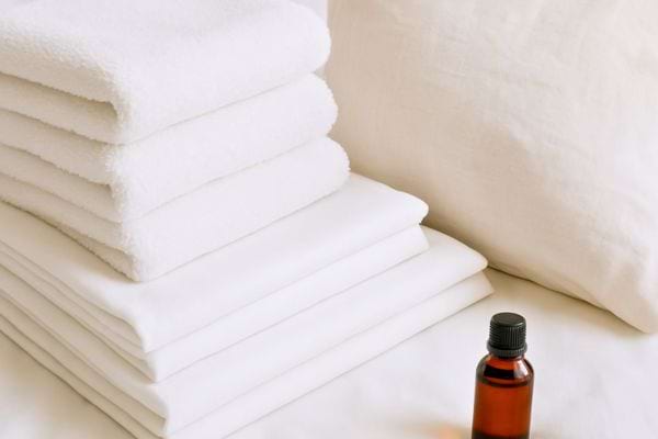Serviettes et draps blancs sont empiles pres d’un petit flacon d’huile essentielle.