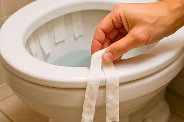 Main posant des bandes de papier imbibees sur le bord des toilettes.