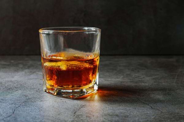 un verre de whisky repose sur une table sombre avec des glacons.