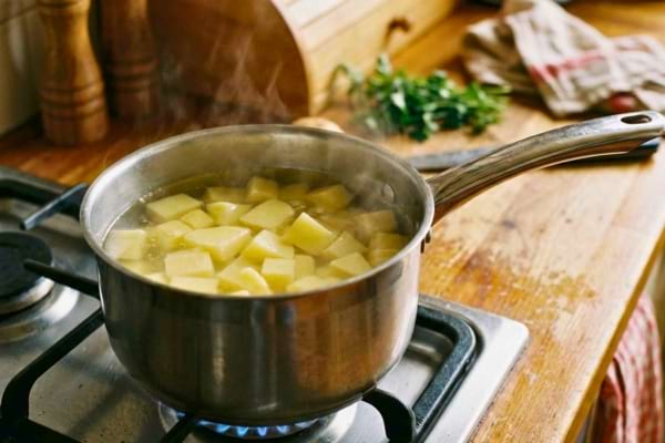 casserole en inox sur un feu doux avec des cubes de pommes de terre crus 