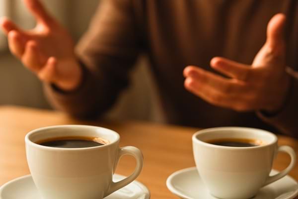 Gros plan sur deux tasses de caf&eacute; sur une table, une personne floue en arri&egrave;re-plan qui gesticule