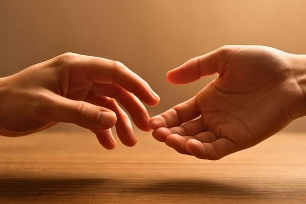 Deux mains pos&eacute;es sur une table en bois, l'une essayant de toucher l'autre mais sans contact complet