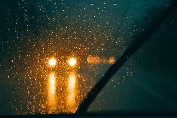 nuit sous la pluie, gouttes sur pare-brise, halos lumineux des phares en face,