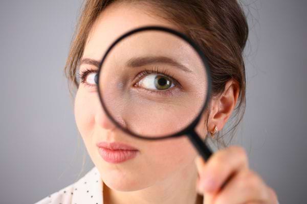 Une femme regarde a travers une loupe qui grossit son oeil de maniere amusante.