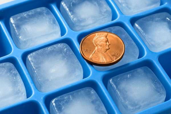 Un bac à glaçons bleu contient des cubes gelés avec une pièce de cuivre posée dessus pour vérifier une éventuelle coupure de courant.
