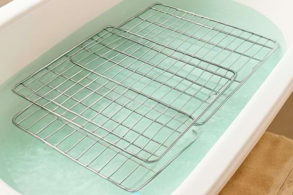 Des grilles de four trempent dans une baignoire remplie d’eau savonneuse pour faciliter leur nettoyage.