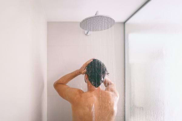 homme sous la douche vu de dos se lavant les cheveux dans une douche moderne avec lumiere naturelle
