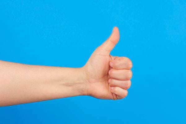 Une main montre un pouce levé devant un fond bleu vif.