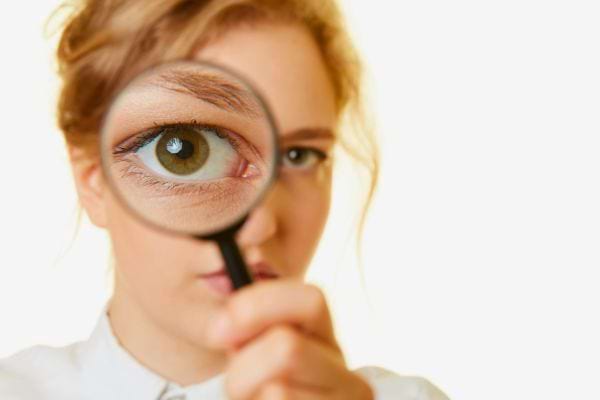 Une femme regarde a travers une loupe qui grossit son oeil vert sur fond clair