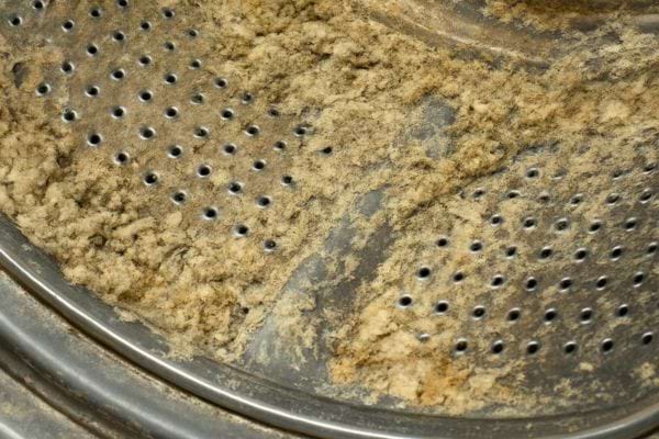 Gros plan sur un tambour de machine a laver encrasse avec depots et residus accumules sur le metal.