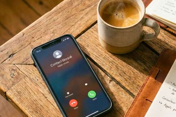 a smartphone on a wooden table with the screen showing an incoming call declined or a "block contact"
