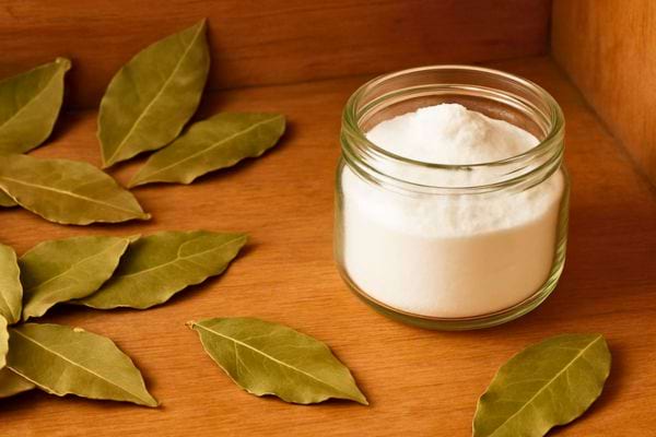 Bol rempli de sel fin entoure de feuilles de laurier seches pose sur une table en bois.
