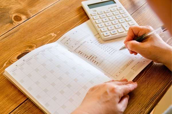 Une personne remplit un carnet avec une calculatrice. La scene montre la gestion du budget personnel.