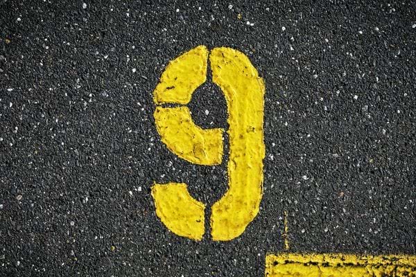 Le chiffre neuf est peint en jaune sur un sol rugueux. Il evoque une etape ou un compte a rebours.
