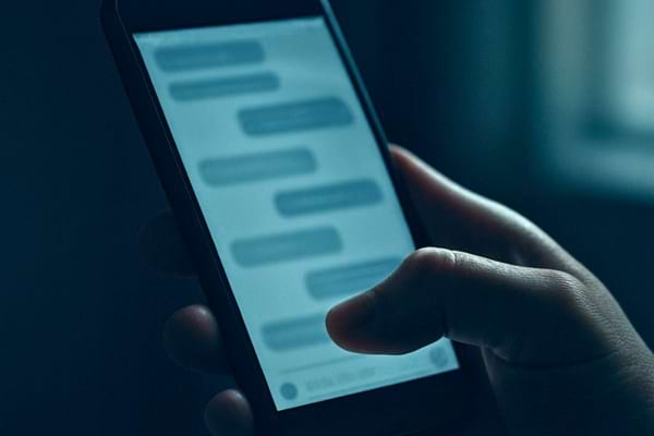 &eacute;cran de t&eacute;l&eacute;phone dans une main avec conversation flout&eacute;e, pi&egrave;ce sombre