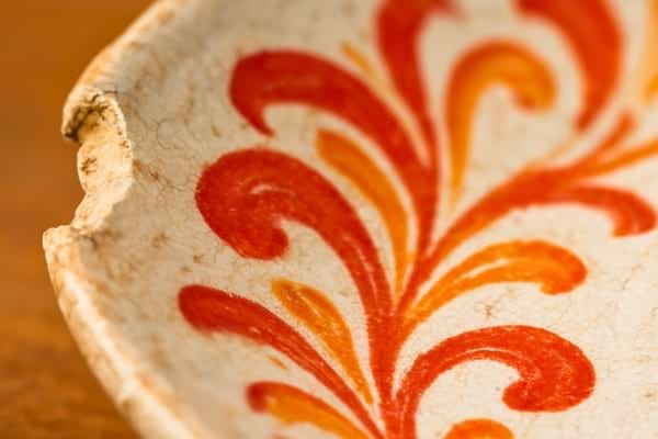 bord d'une assiette ancienne &eacute;br&eacute;ch&eacute;e. On voit la texture de la fa&iuml;ence et un motif rouge vif et orange