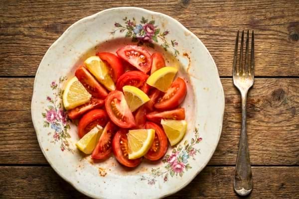 Une table dress&eacute;e vue de dessus. Une belle assiette vintage contient une salade de tomates avec des quartiers de citron (aliments acides)