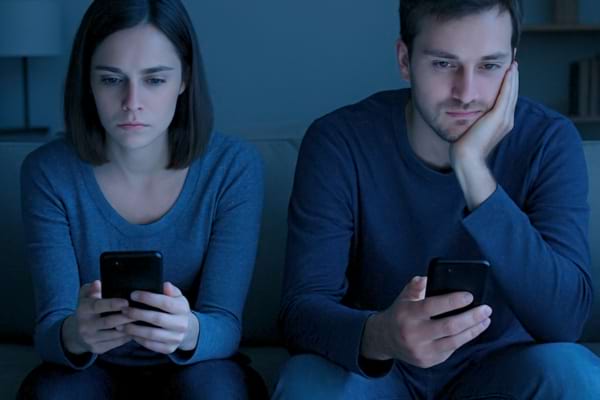 Un couple assis sur un canap&eacute; chacun regardant son propre t&eacute;l&eacute;phone