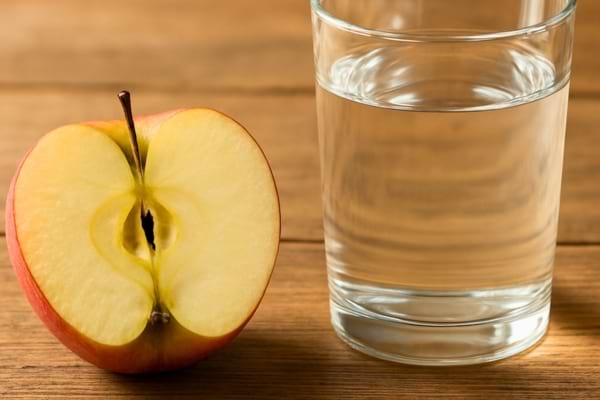 ne belle pomme coup&eacute;e en deux pos&eacute;e sur une table en bois rustique &agrave; c&ocirc;t&eacute; d'un verre d'eau,