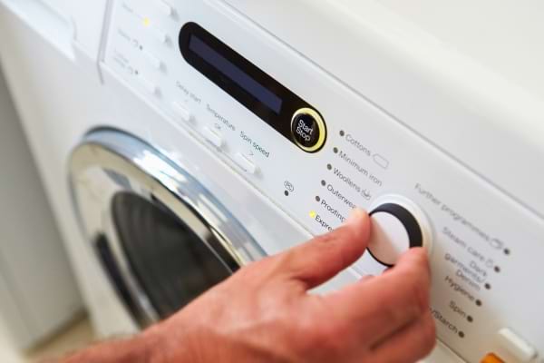 main r&eacute;glant le d&eacute;part diff&eacute;r&eacute; sur le panneau d&rsquo;un lave-linge,