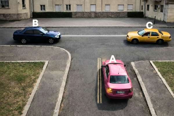 une intersection en T, trois voitures colorées (bleue sur la route principale, rose sur la branche qui se termine, jaune à droite)