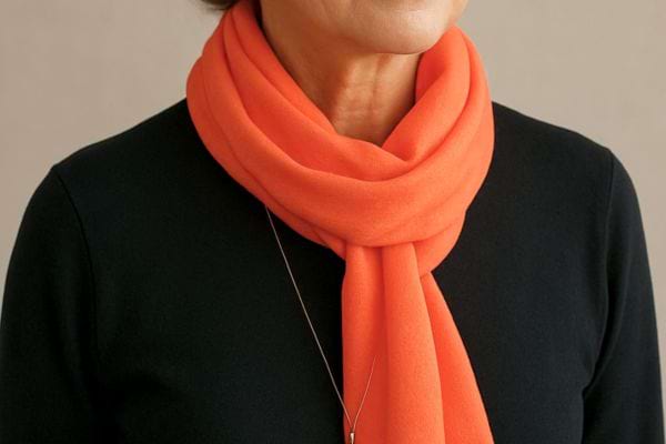 Gros plan sur une echarpe orange portee autour du cou contrastant avec un haut sombre