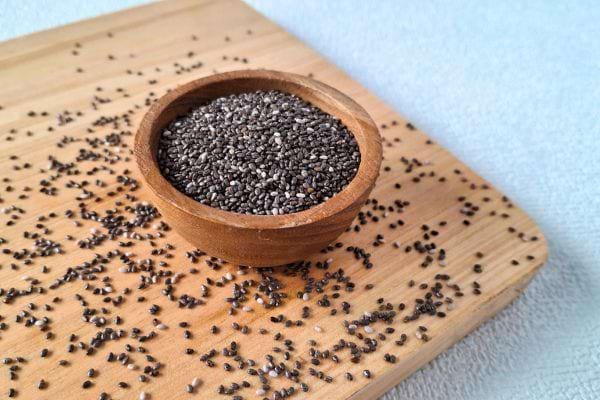 graines de chia dans un petit bol en bois sur planche claire