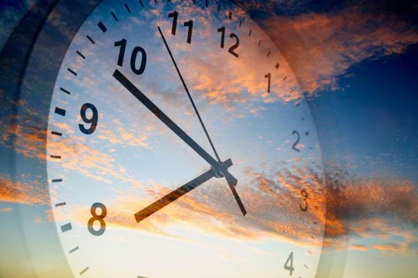 horloge transparente superposee a un ciel colore evoquant le temps qui passe et la fin de journee