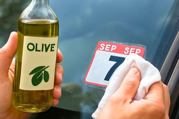 Une main nettoie une vignette collee sur une vitre avec de l huile d olive et un chiffon doux.