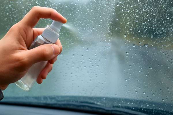 main tenant un pulverisateur applique un spray sur un pare brise couvert de gouttes de pluie