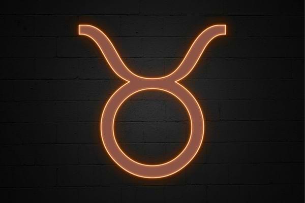 Le symbole du taureau en neon orange apparait sur un mur sombre. Il evoque stabilite et materiel.