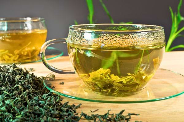 tasse en verre de the vert infuse avec feuilles de the sechees autour