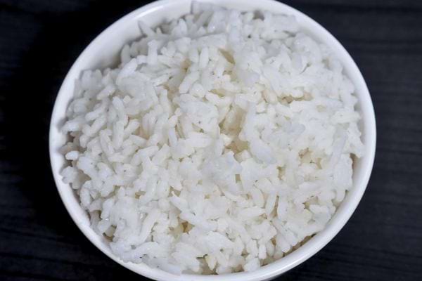 un bol blanc rempli de riz blanc cuit est pose sur une surface sombre