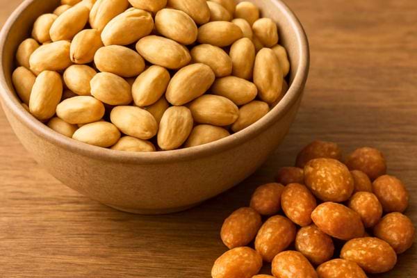 un bol rempli de cacahuetes grillees avec quelques arachides enrobees posees sur une table en bois