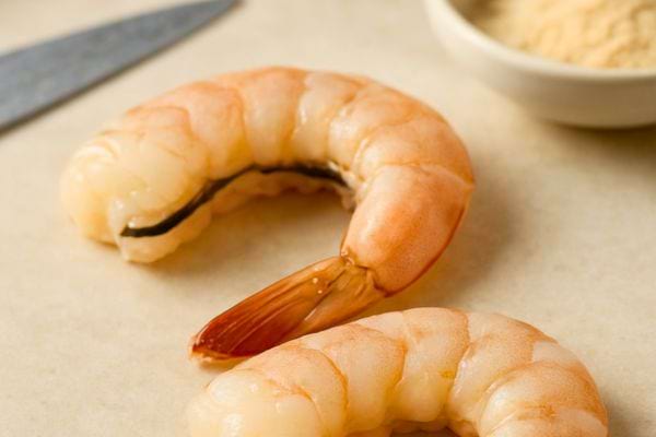 deux crevettes cuites roses posees sur un plan de travail avec queue intacte