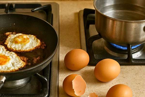 oeufs au plat dans une poele sur gaz avec casserole deau bouillante et oeufs crus a cote