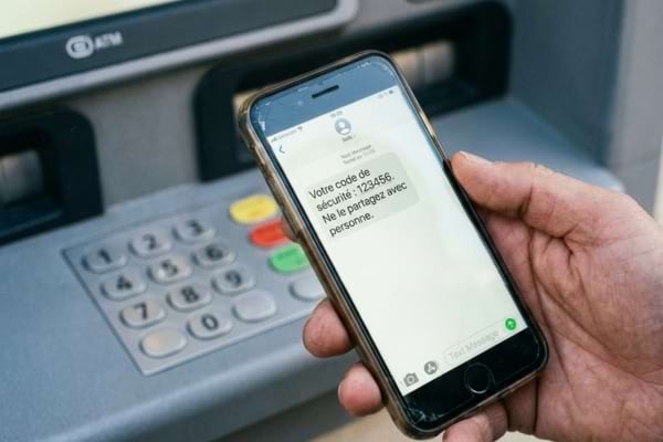 Une main tient un smartphone affichant un SMS avec un code de s&eacute;curit&eacute; &agrave; 6 chiffres