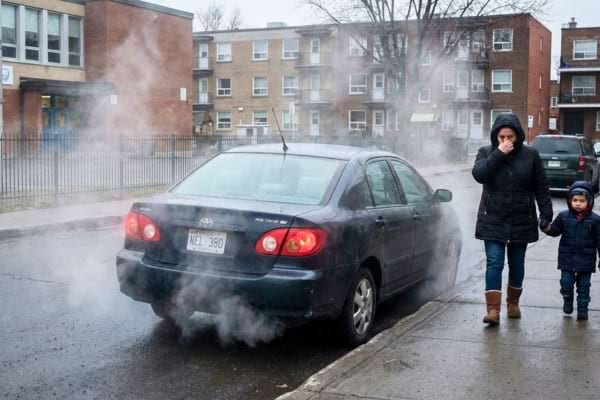 A car parked with engine running (smoke visible) near a school gate. A child with a colorful backpack is walking by, covering their nose