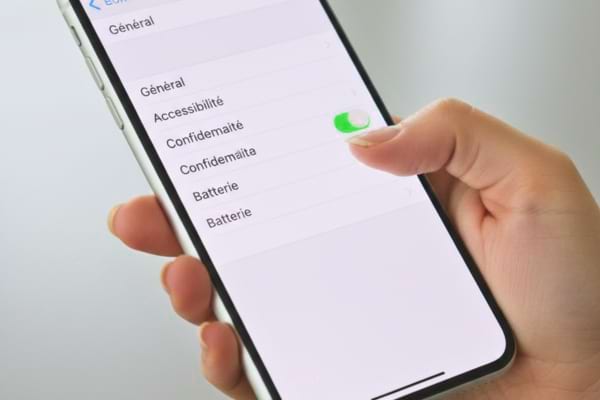 &eacute;cran affiche les r&eacute;glages iOS avec le doigt d'une femme sur le point d'activer un bouton vert.