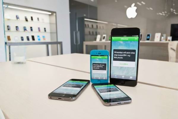 Old iPhone models (iPhone 5, 5c, 6) lined up showing WhatsApp compatibility warning message on screens